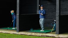 Two golfers hitting at the driving range, one in the follow-through position and one at set-up