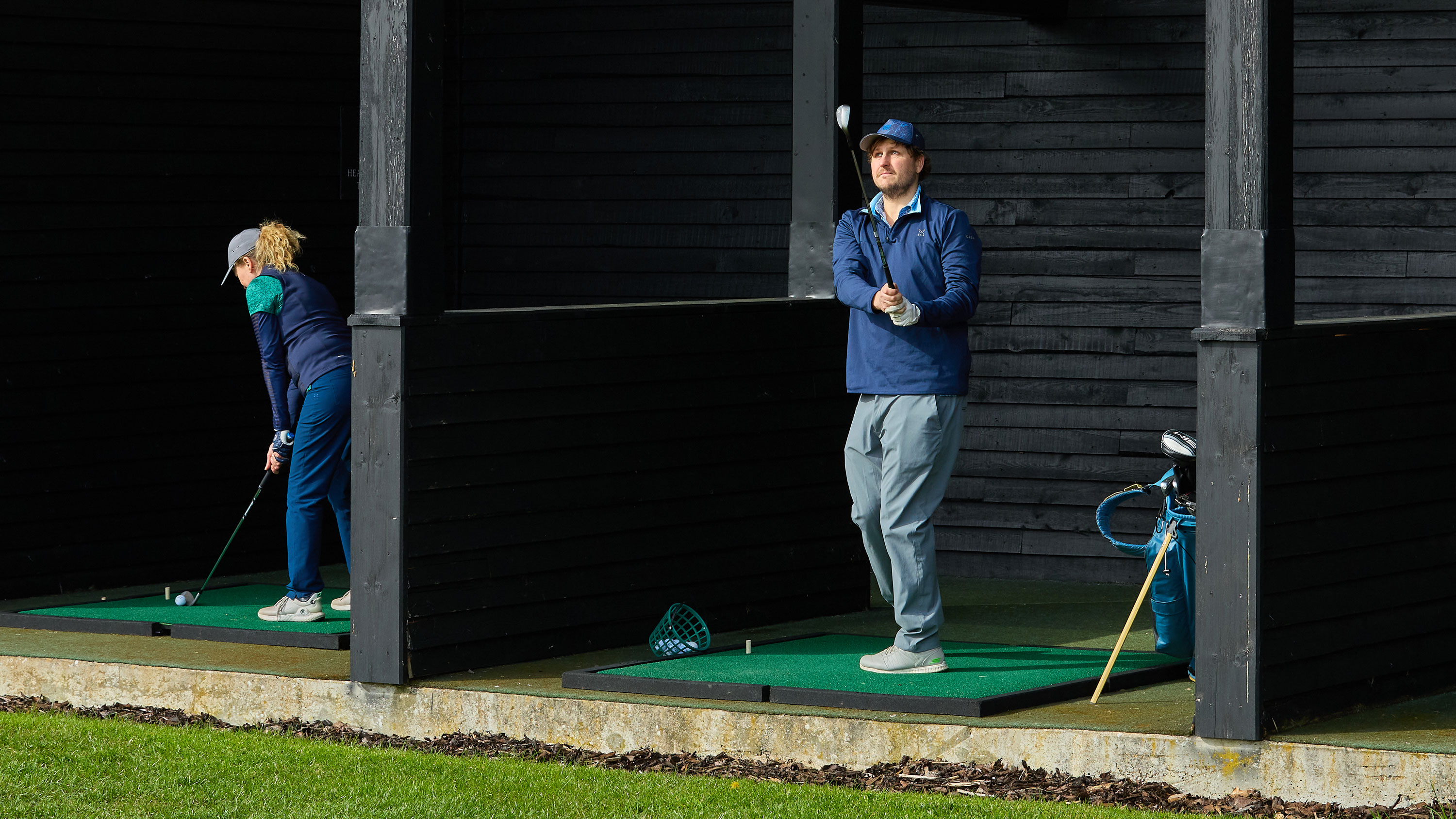 Two golfers hitting at the driving range, one in the follow-through position and one at set-up