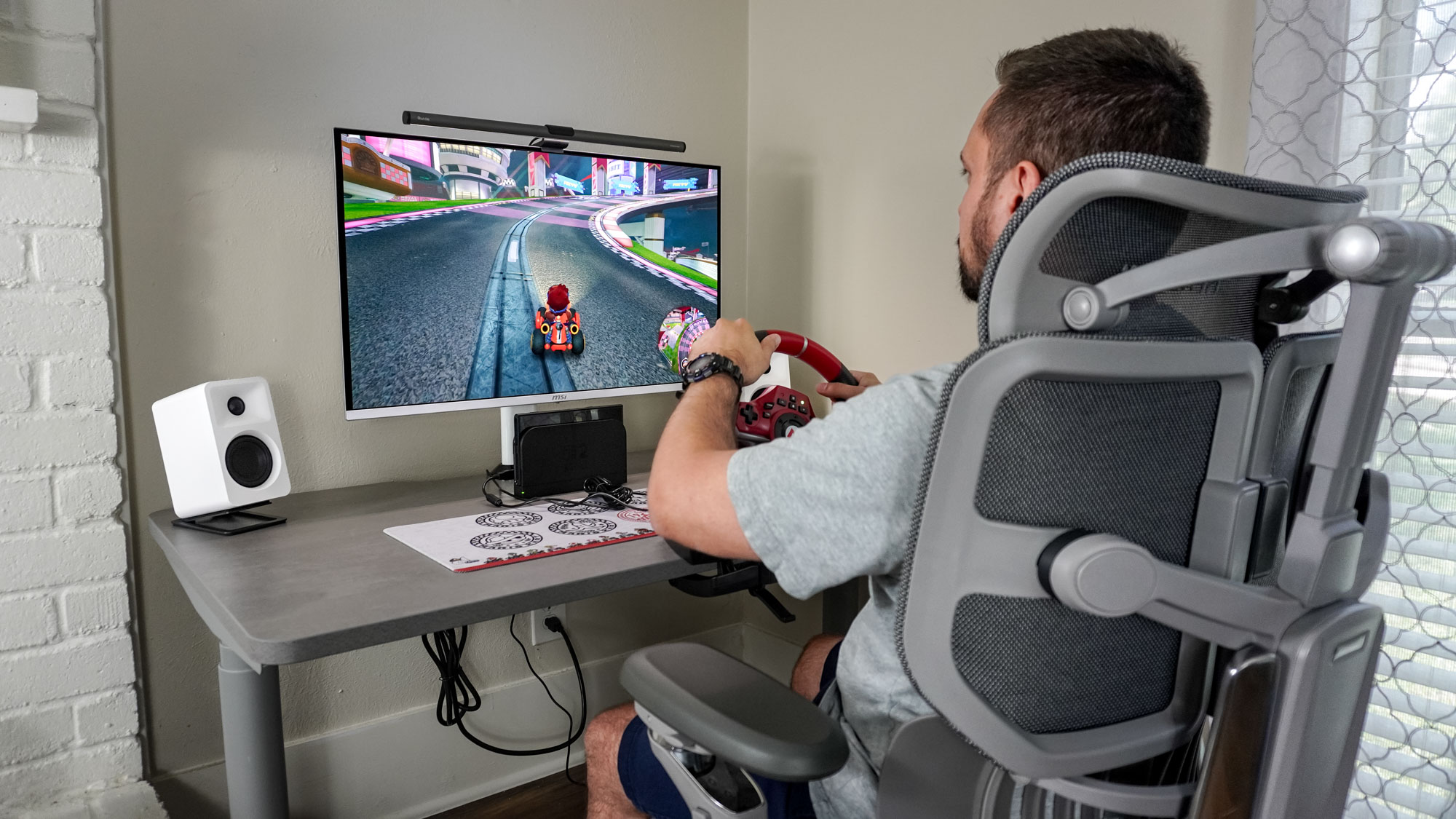 A person sitting at desk in an office chair playing Mario Kart World with the Hori Pro Deluxe racing wheel