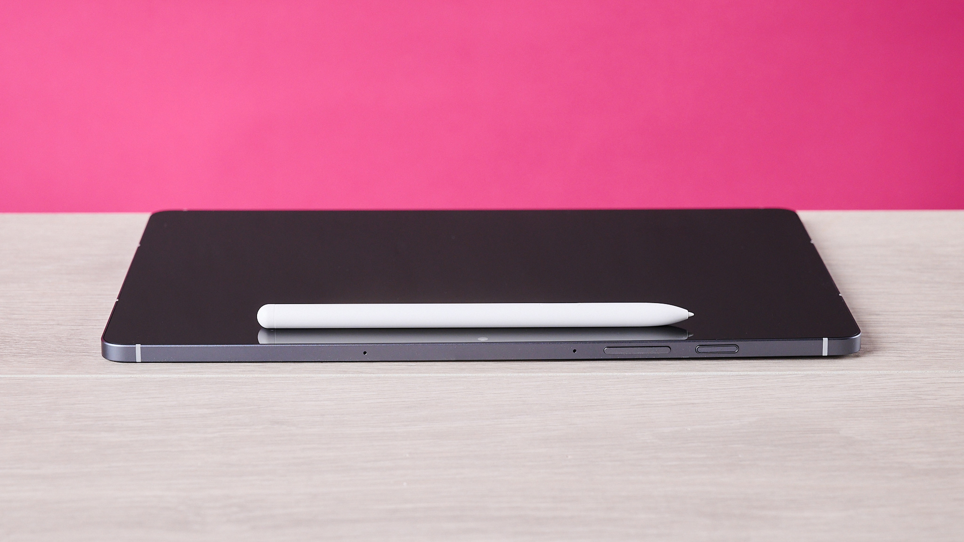 The Samsung Galaxy Tab S10 FE laying flat on a table with the S Pen on top of it and in front of a pink background.