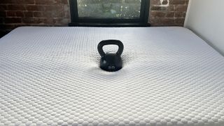 Image shows a 55lb black weight placed in the middle of our review model of the Layla Essential Mattress during a firmness test
