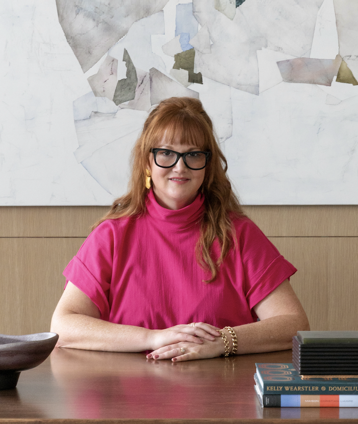 A headshot of a woman with auburn hair and glasses wearing a pink top
