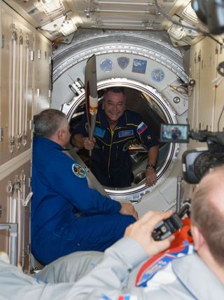 Russian cosmonaut Mikhail Tyurin holds the Olympic torch as he enters the International Space Station.