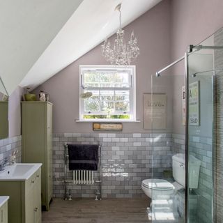 a bathroom with top half of wall in blush pink paint and bottom half with grey and white tiles, pale timber floor and green cabinets