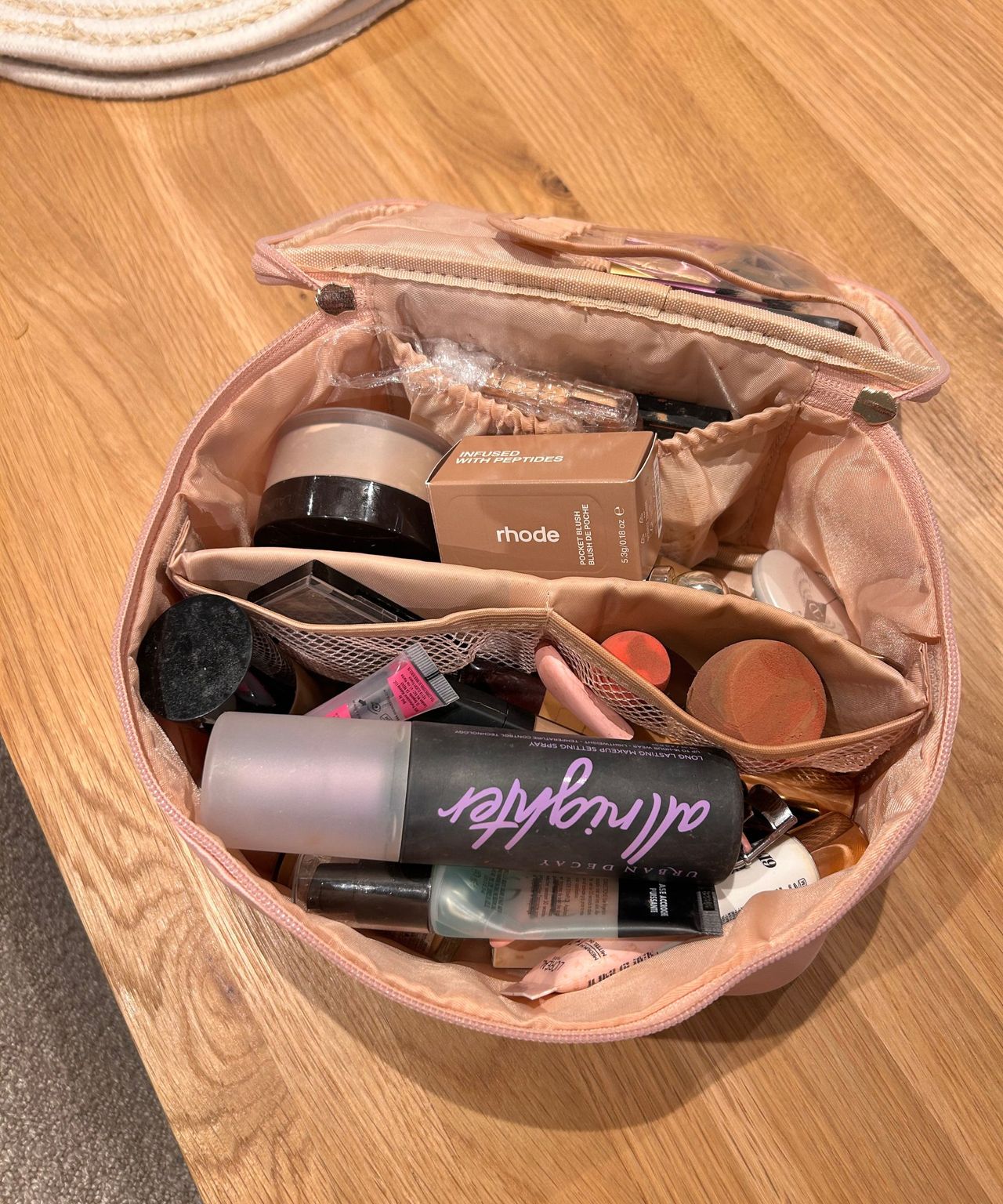 Messy pink makeup bag with lots of products in open and on a table