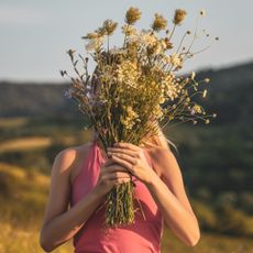 Woman holding a bouquet of dried flowers in front of her face while standing in a meadow