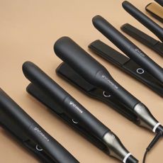 5 black GHD hair straighteners led on a tan background