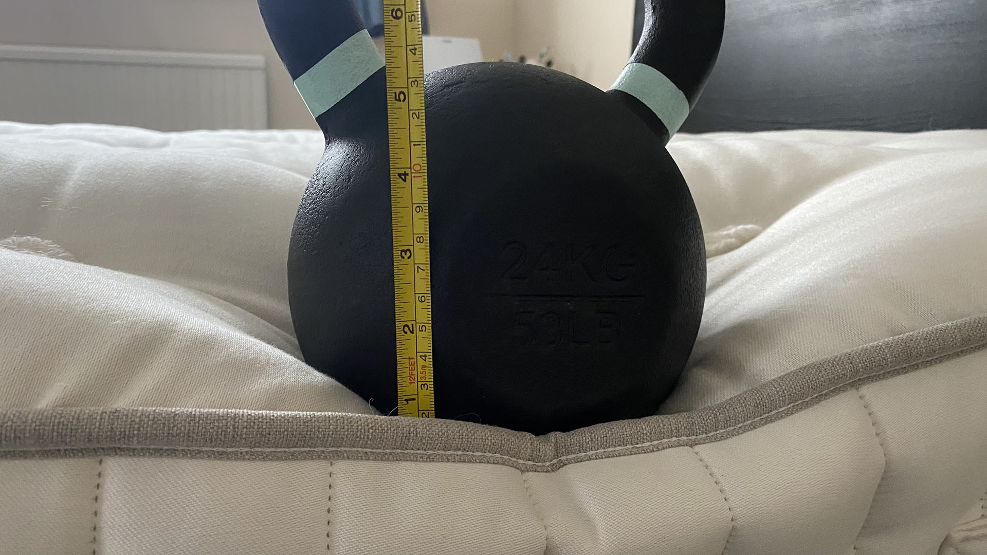 A 24kg kettlebell sitting on the edge of the Simba Earth Escape mattress, with a tape measure showing how much the mattress sinks