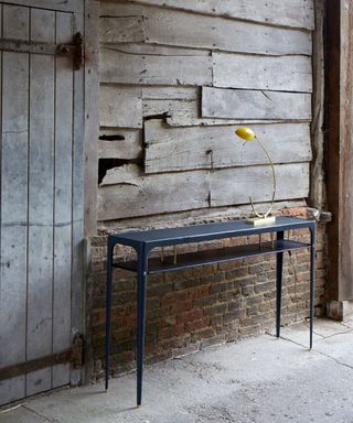 Ochre leather console table in front of rustic wooden wall with yellow table light