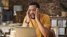 A man massages his temples as if he has a headache while looking at his laptop.