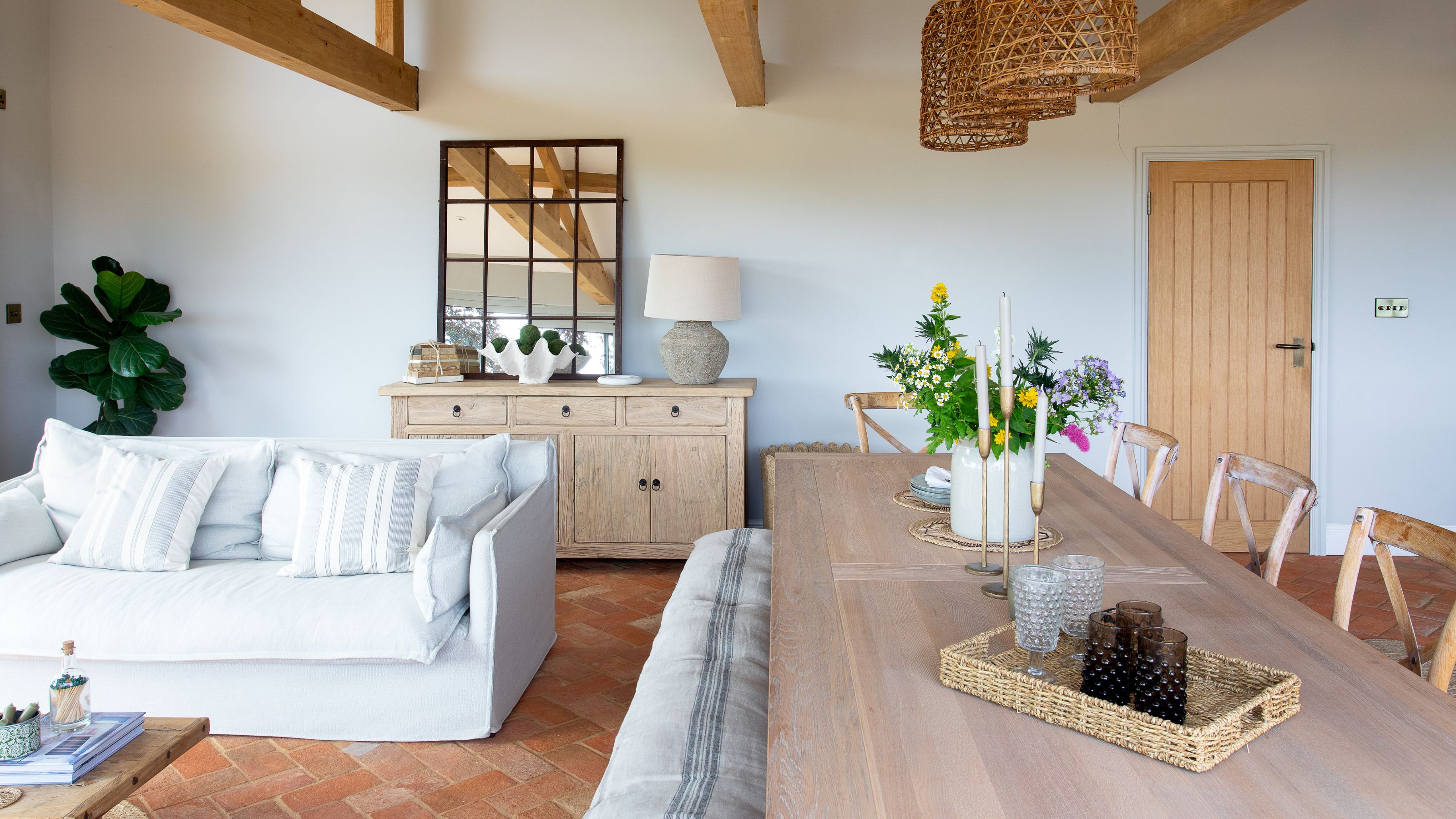 Open plan dining and living space, with neutral tones and tiled floor. There's a wooden dining room and a white snuggly sofa