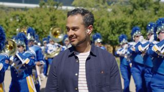 A man wearing a pair of AirPods with a marching band around him