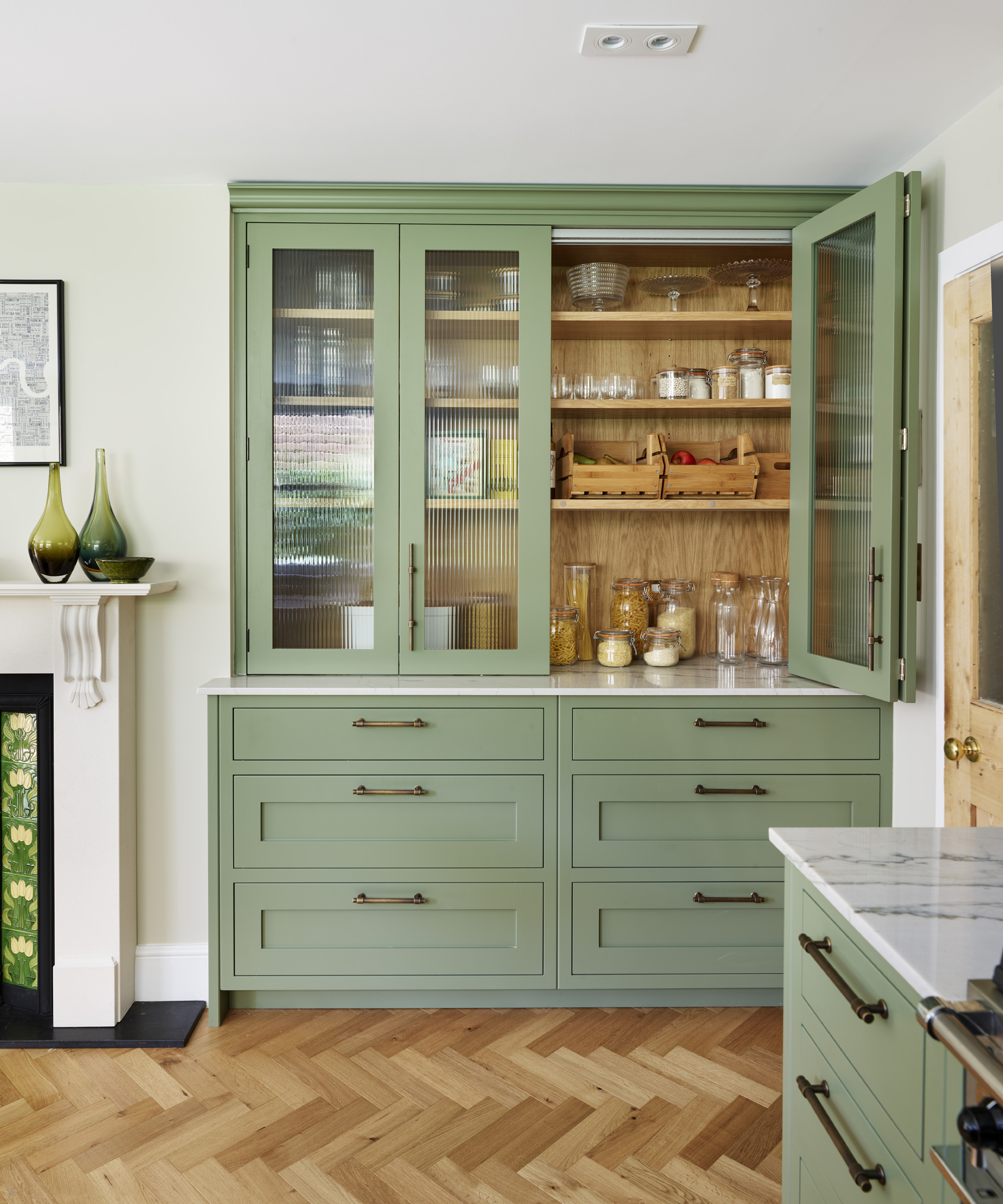green, glass and wood kitchen pantry built into wall with doors, drawers and shelving