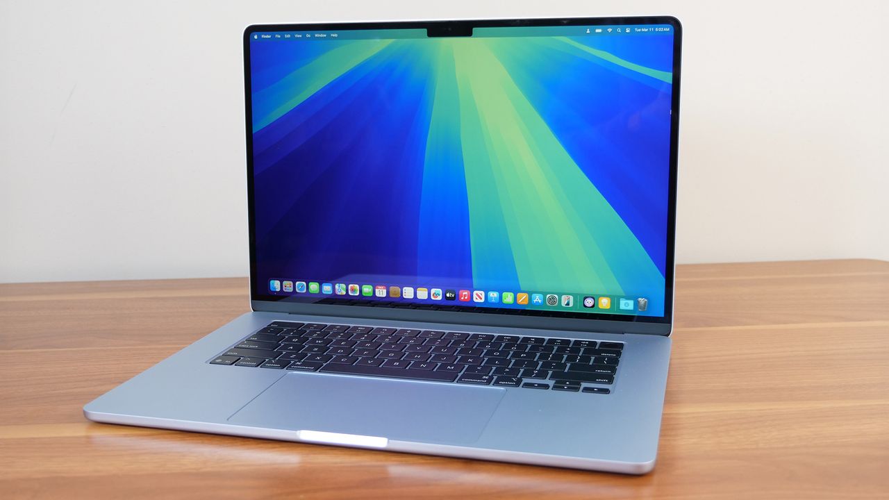 An open and powered on silver laptop on a wooden table, showing an image of blended blue and green chunky lines on its screen.
