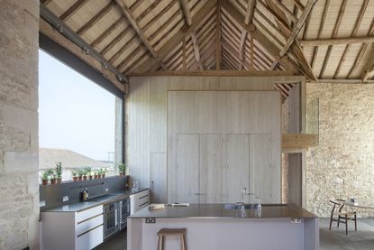 Tall barn kitchen with light wood panelling and a panoramic window looking into the countryside
