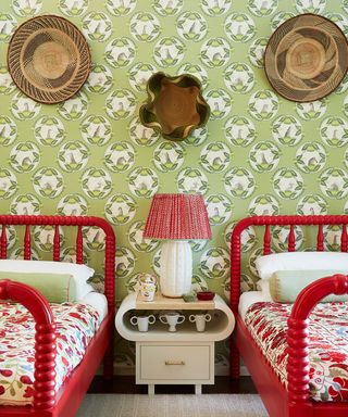 A green bedroom with cute red painted twin beds, green and white wallpaper and a red bedside lamp