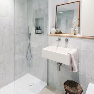 shower with vertical tiles next to white sink and shelf with mirror