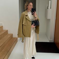 Anouk wears a trench coat, sweater, silk pants, and a toteme clutch.