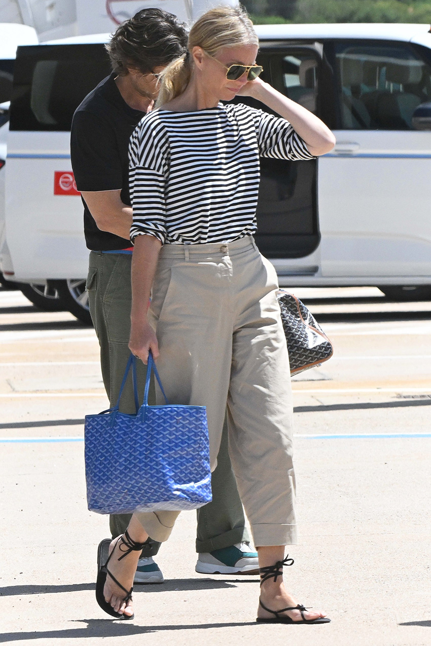 Gwyneth Paltrow wearing a striped tee with khaki pants, a Goyard tote, and ankle-wrap sandals in Sardinia