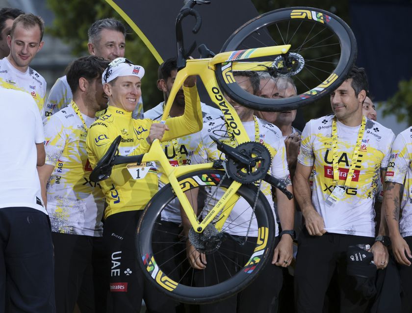 Tadej Pogacar stands on the Tour de France podium holding his bike aloft