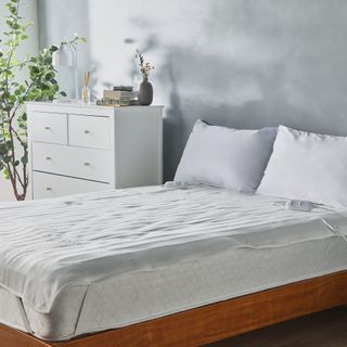 white electric blanket on bed with wooden base and white chest of drawers