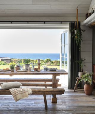 Dining area with wooden table and benches and sea view in Cornish coastal newbuild