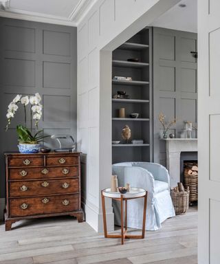 living room with grey panelled walls and potted white orchid on wooden antique chest