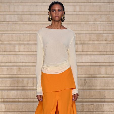 A woman at the TOVE spring/summer 2025 show wears an orange skirt, a beige long-sleeve shirt