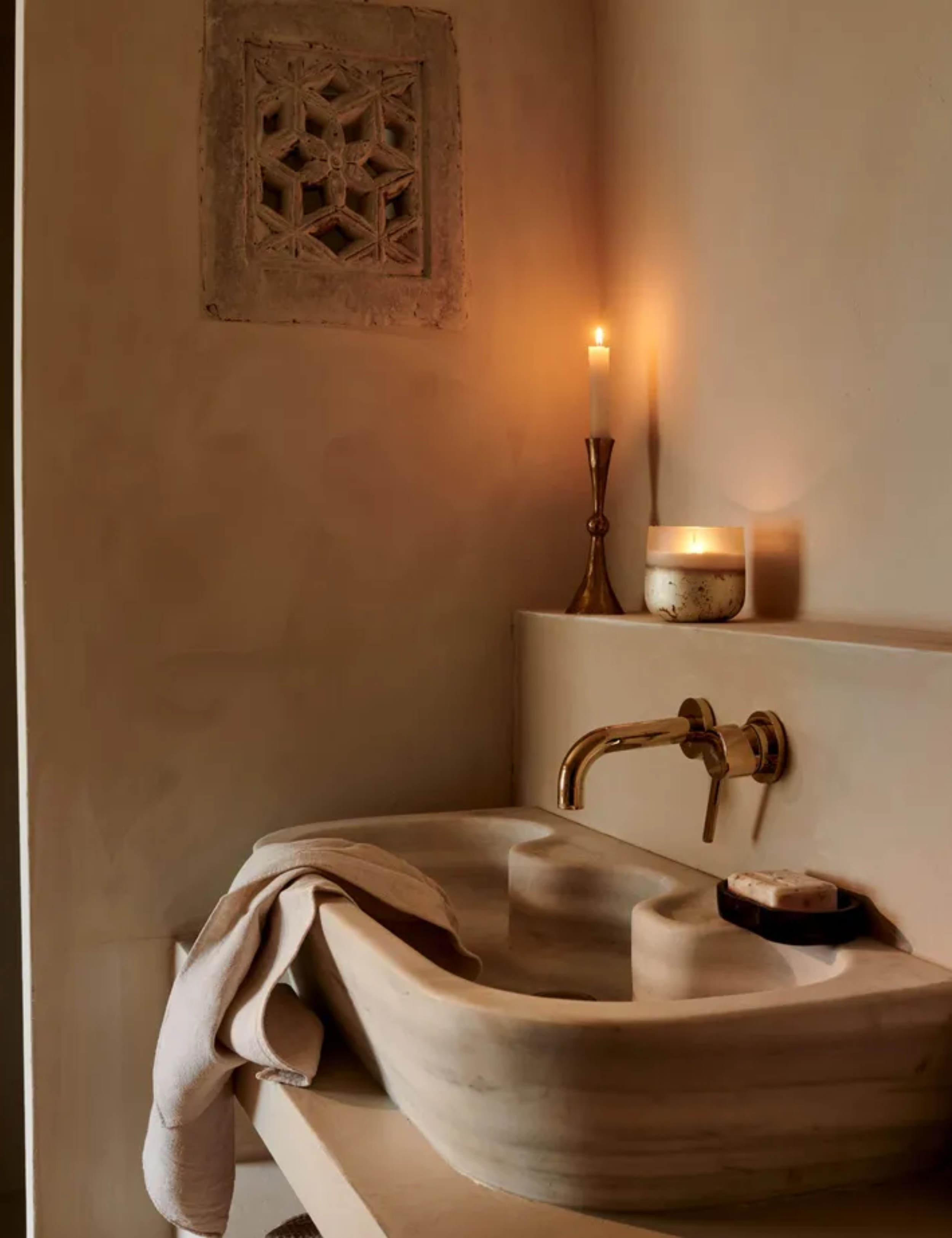 A carved stone sink in a paster-wall bathroom. A candle lit on the ledge above.