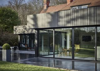 A backyard of an extended house that has large doors and windows.