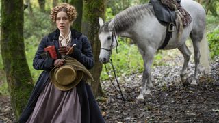 Ann Walker (Sophie Rundle) in a blue coat in the woods alongside a white horse in Gentleman Jack.