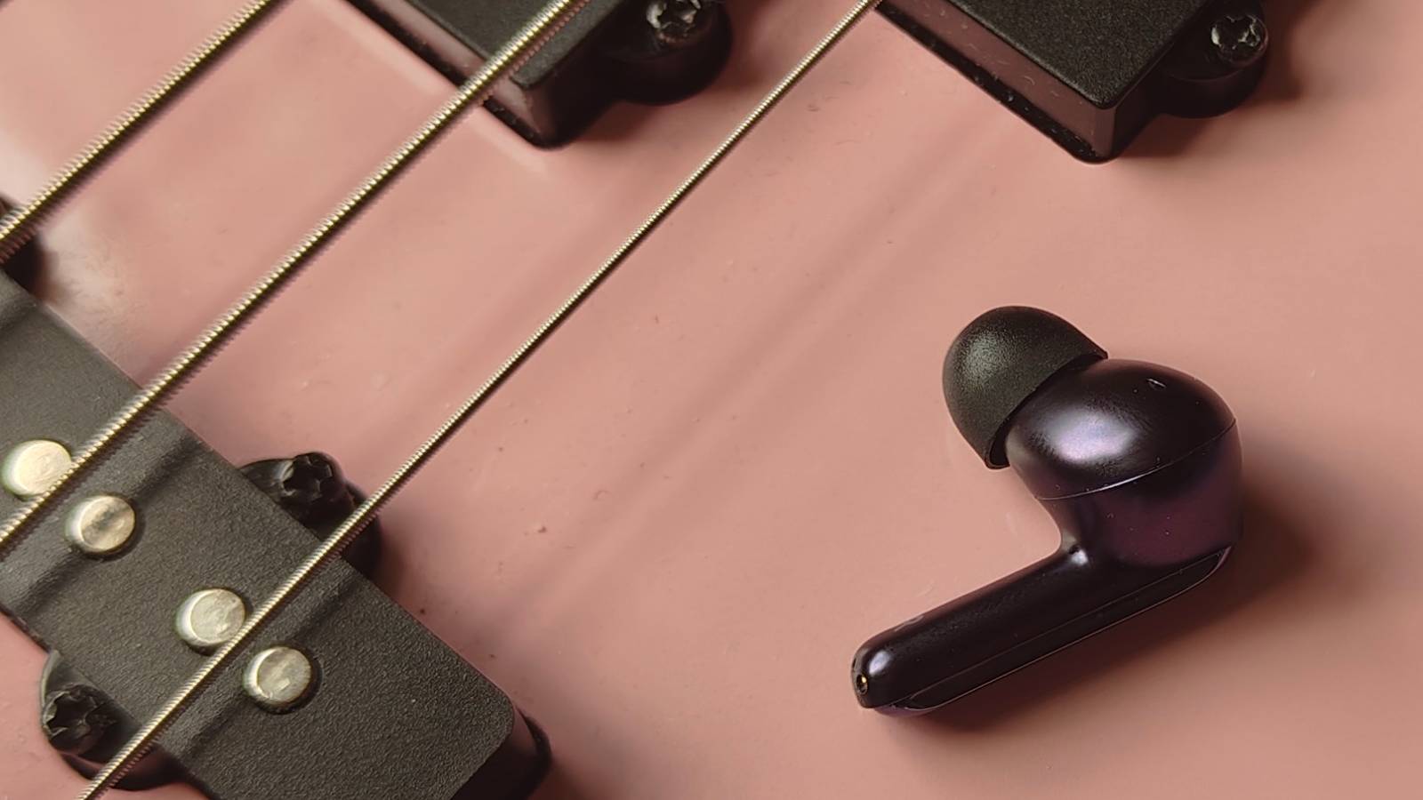 The Creative Aurvana Ace 3 bud on a pink bass guitar.