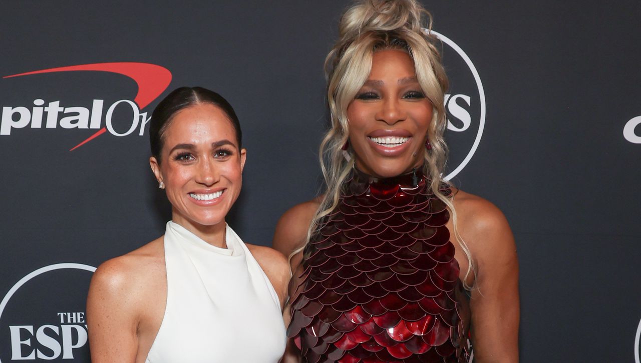 Meghan Markle stands next to Serena Williams on the red carpet for the 2024 ESPY awards wearing a white halter dress and diamond earrings