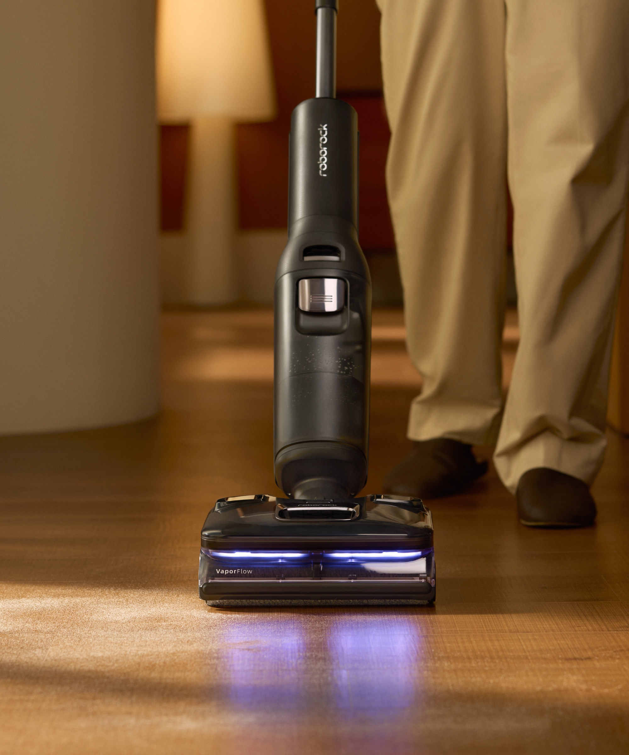 Roborock F25 Ultra vacuum-mop on wooden floor with person's legs pictured behind.