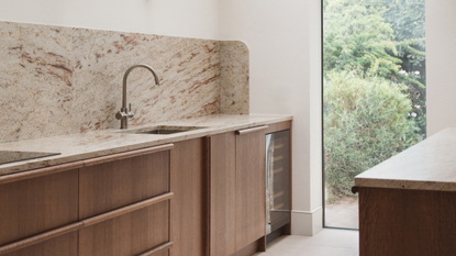 A galley kitchen with wooden cabinetry, stone counters and white walls