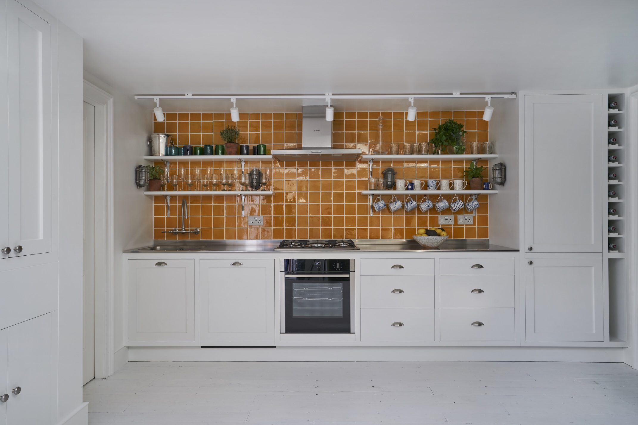 A one wall kitchen in all white with a bright orange square tile splashback