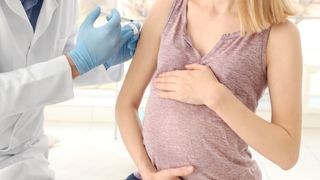 Gloved doctor giving a pregnant woman a vaccine