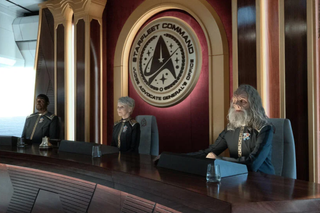 three people in suits stand in front of the starfleet command logo during a tribunal, in the show 'star trek: strange new worlds'