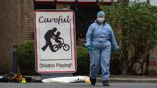 A sign saying 'Careful: children playing' with a person in a blue hazmat suit, mask and hairnet in the background