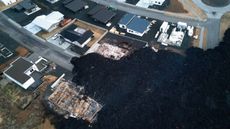 aerial view showing houses in Grindavik destroyed by lava that has since solidified and turned black.