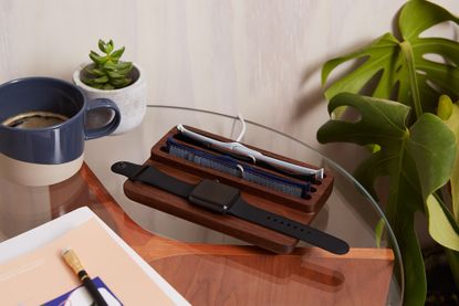 A glass table with a plant, coffee mug, magazine and wooden Apple Watch charger – one of the best Apple Watch accessories