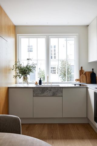 White marble kitchen counter with white and wooden cupboards by a large window.