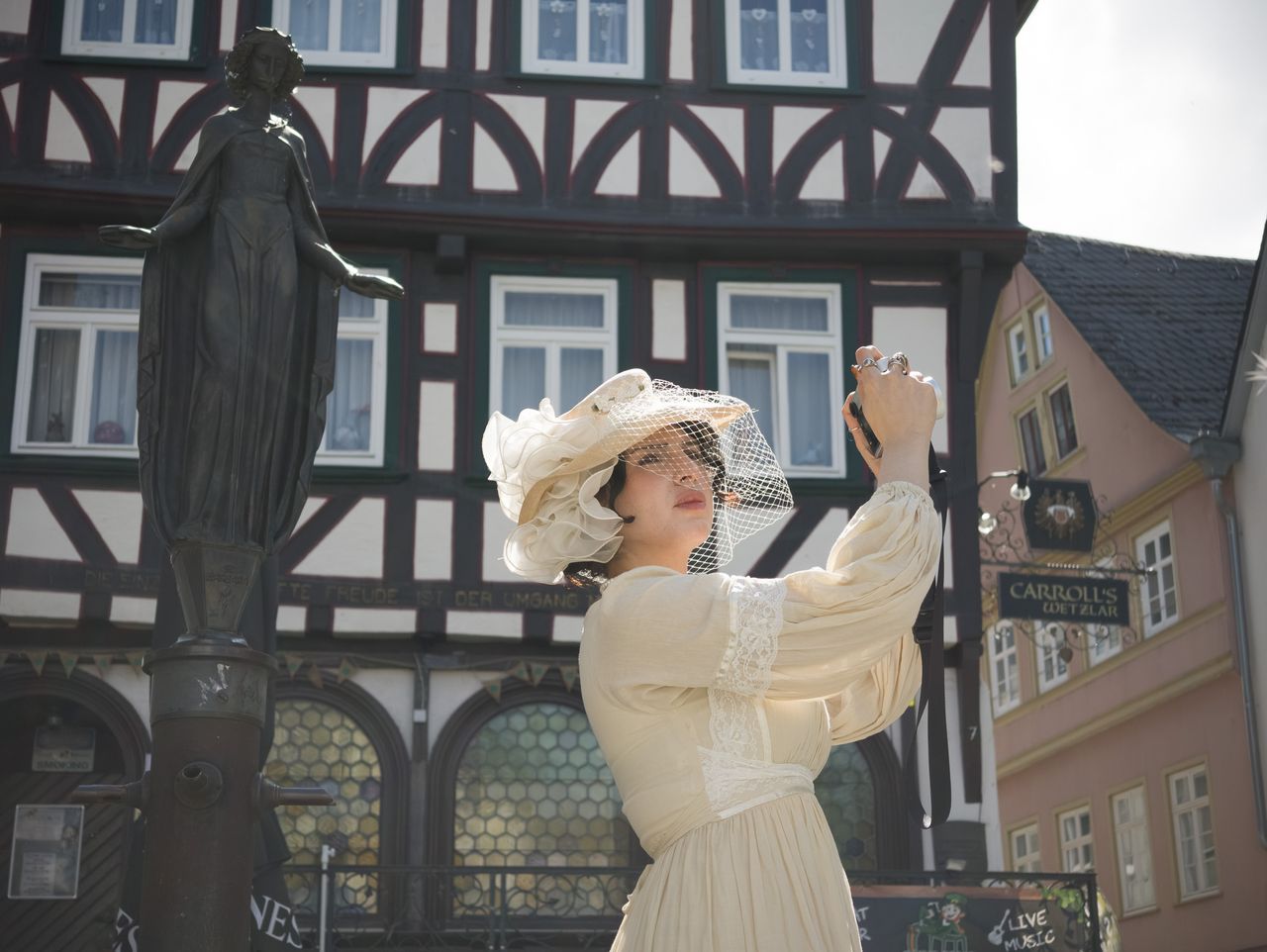 Insta360 Luna Ultra sample gallery: lady in period clothing holding a Leica camera, in quaint German town,