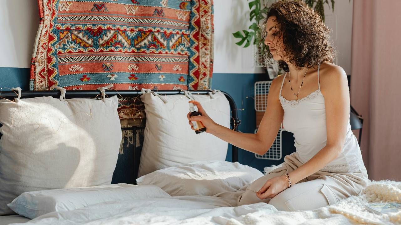 A woman sitting on her bed and spraying it with essential oils