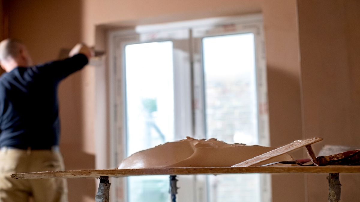 Brown wall plaster on stand with man in background plastering wall