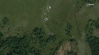 a satellite photo of a plane crash site surrounding by grassy fields and trees, with 20 or so vehicles nearby.