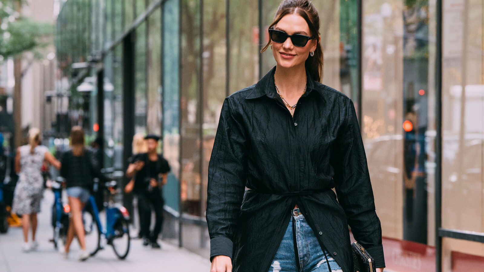 woman wears black maxi top/jacket and jeans while walking on a busy city street