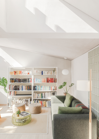 A cream living room with a dark green sofa and simple bookcases.