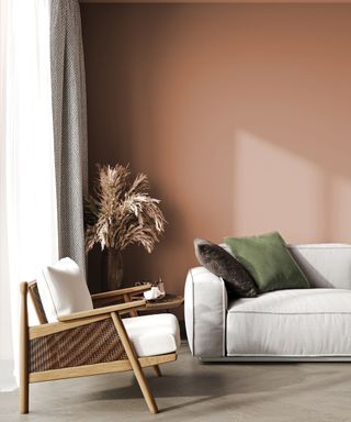 living room with terracotta walls, neutral sofa, woven armchair and dried flowers