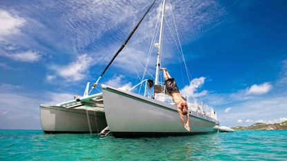 A mature man enjoys his vacation by diving off of the deck of a catamaran sail boat into the turquoise waters of the Caribbean on a beautiful day.